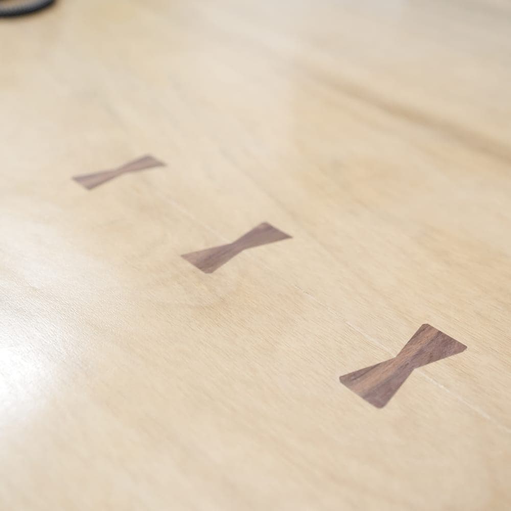 Close-up of three dark wood bowtie inlays set into a light live-edge tabletop