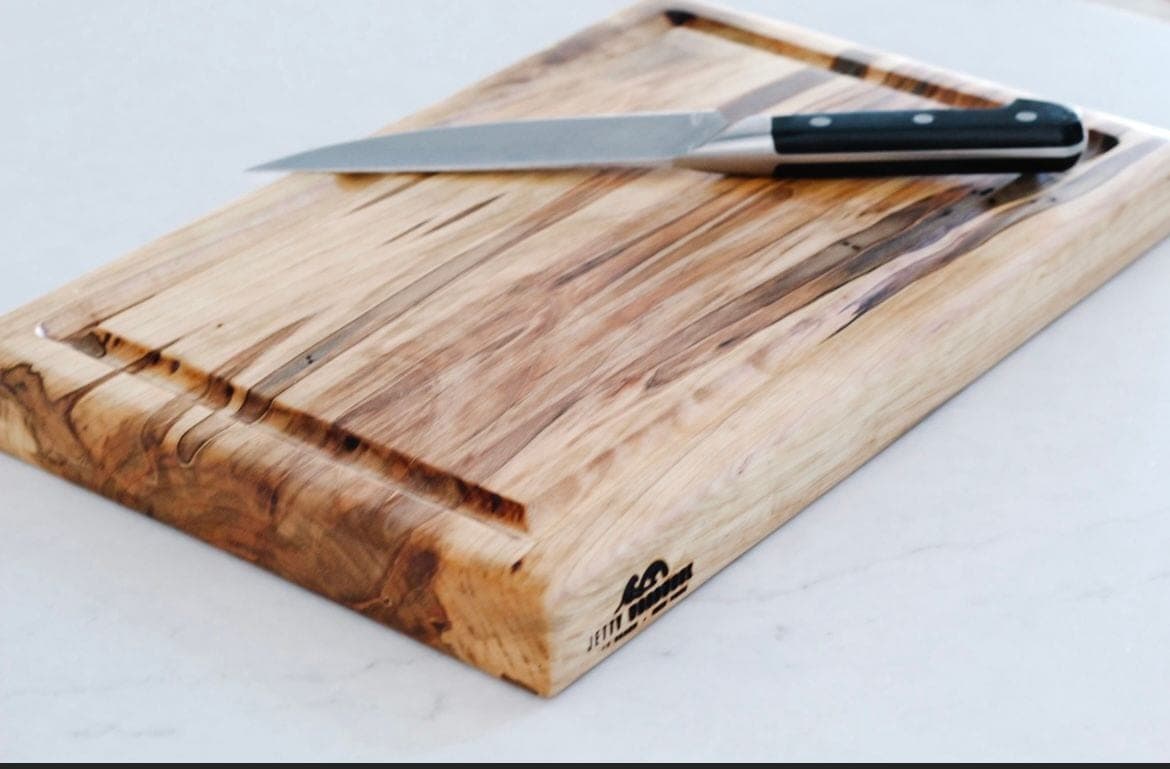 Light wood cutting board with dark streaks and a juice groove, a chef's knife on top