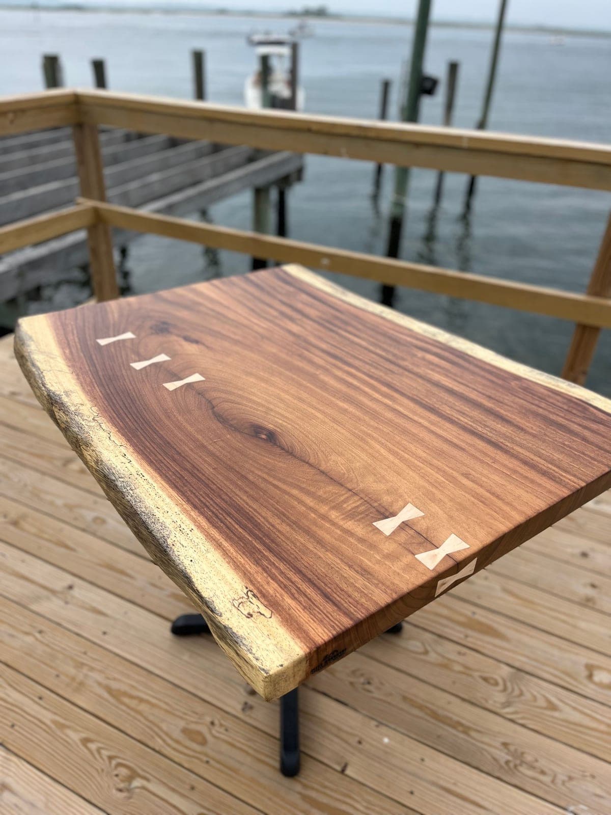 Live-edge slab table with light bowtie inlays on a waterfront deck
