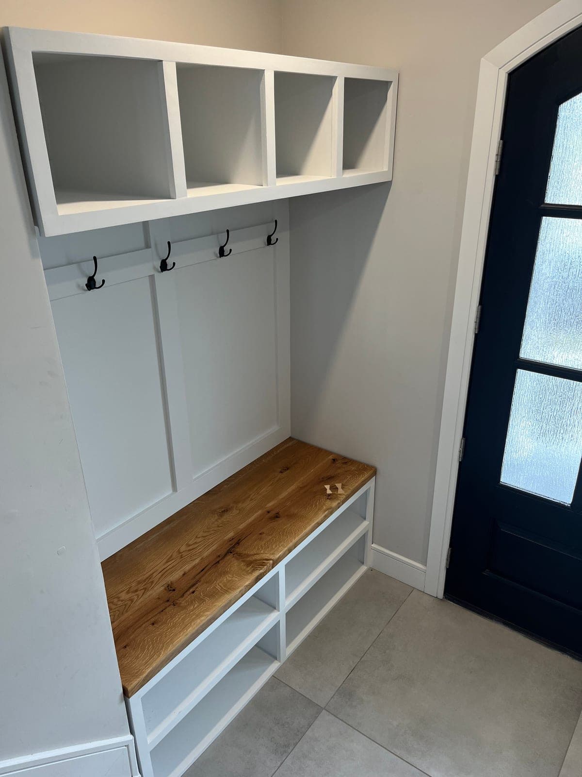 White mudroom built-in with a wood bench seat, cubbies above, coat hooks and shoe shelves